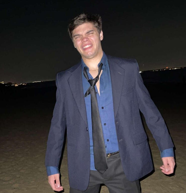 Treverse standing on a beach in a raggedy suit.